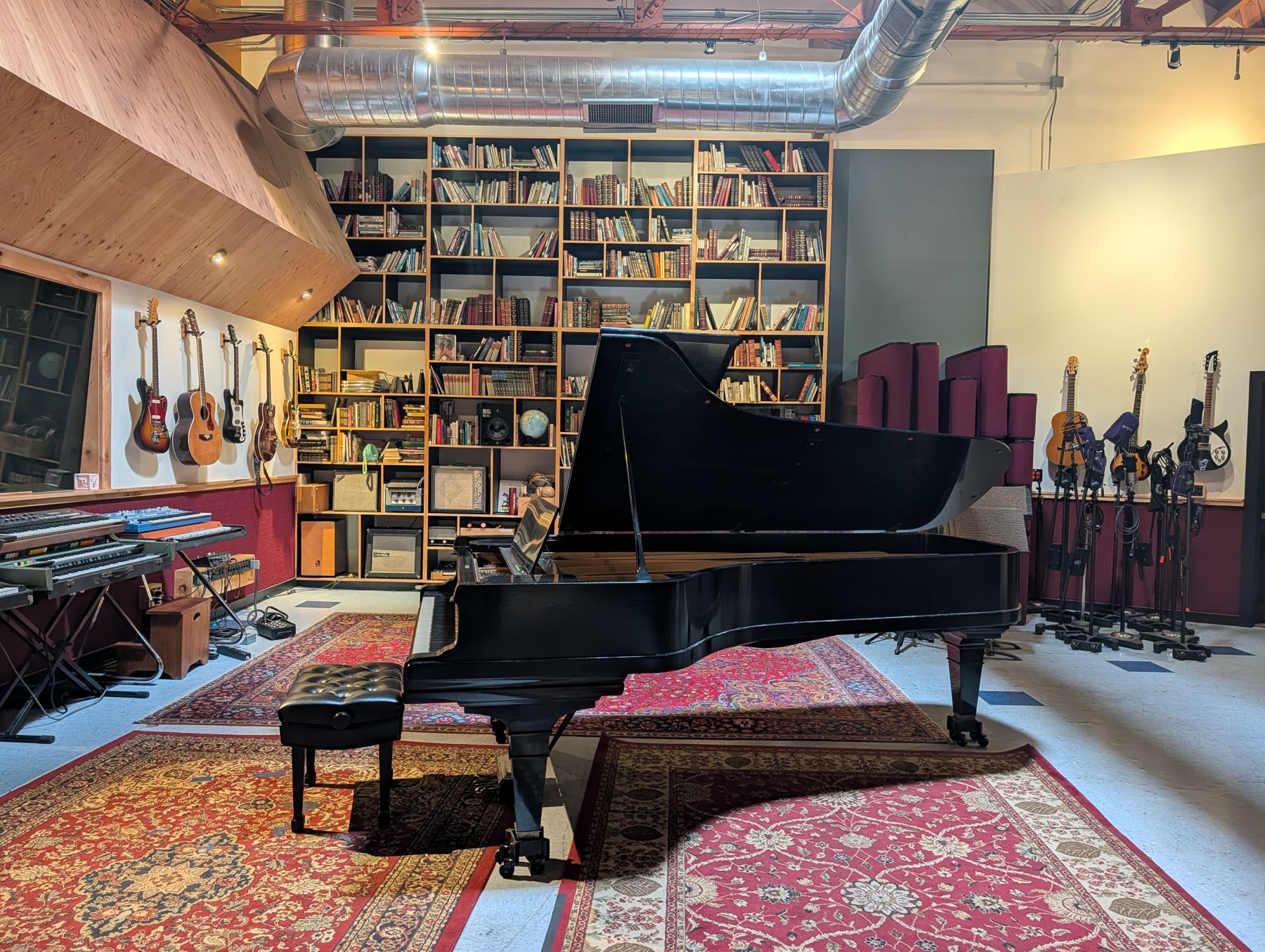 The live room at Tiny Telephone: a black grand piano on Persian rugs in front of a wall of books and hanging guitars.